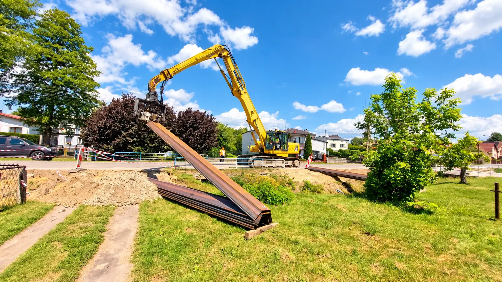 Wibromłot na Komatsu utrzymuje długą grodzicę stalową nad składem kolejnych grodzic.