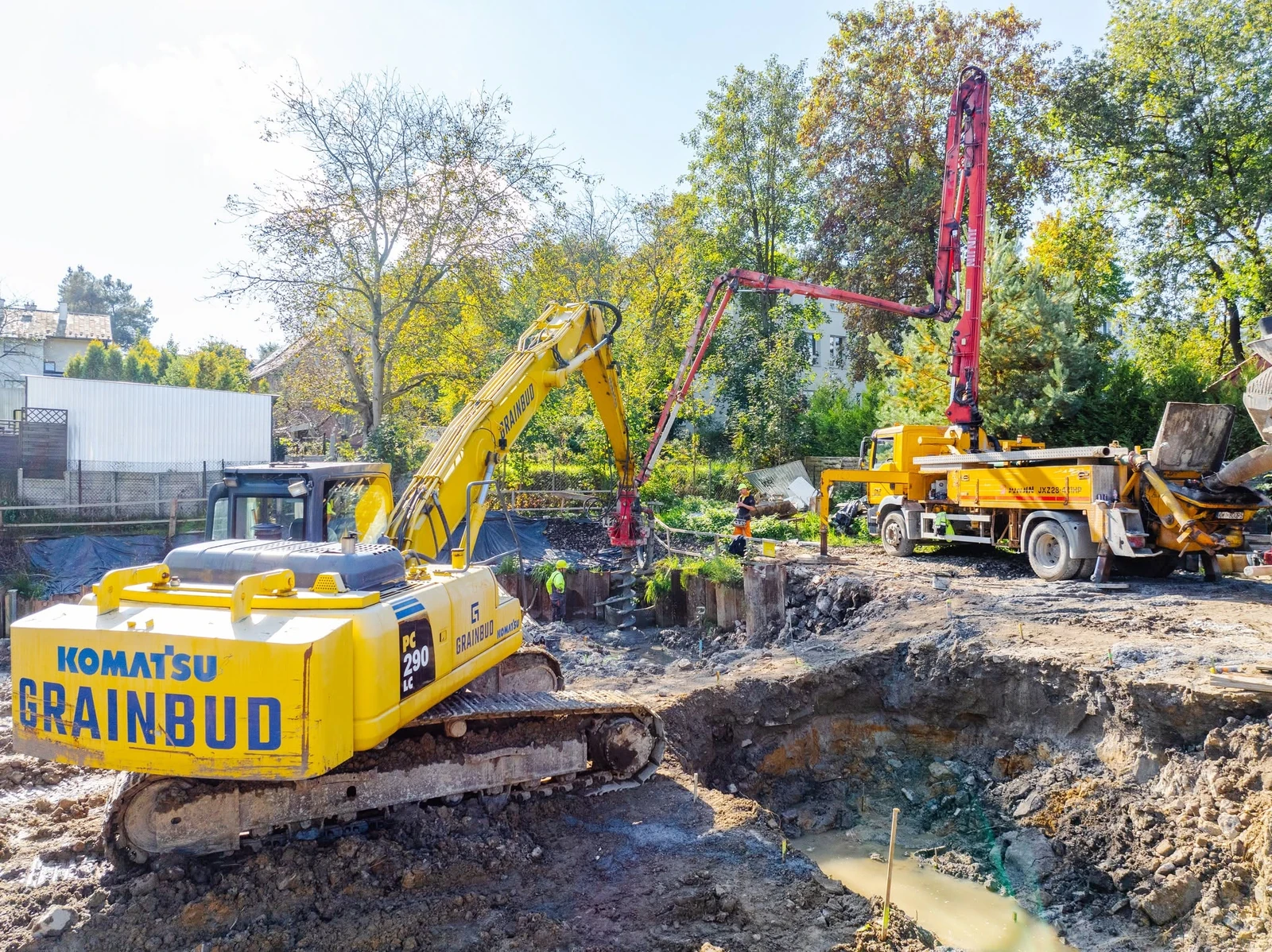 Komatsu PC290 z wiertnicą i pompa do betonu przy wykopie otoczonym stalową obudową.