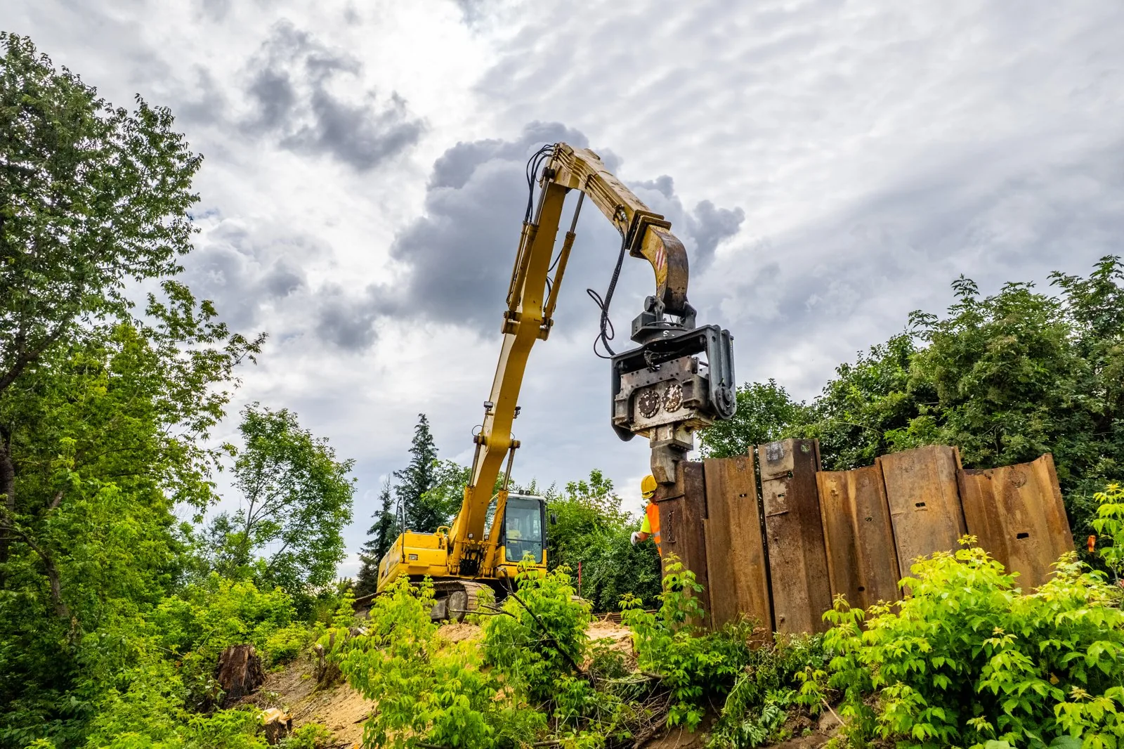 Wibromłot na koparce Komatsu przy pionowych grodzicach stalowych, widok od dołu.